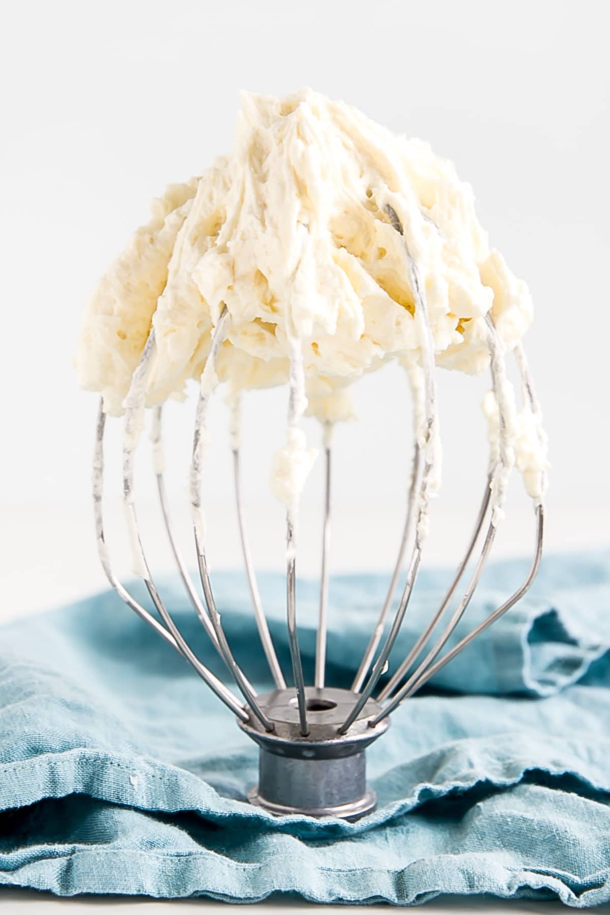 Ermine Frosting (also known as flour buttercream or heritage frosting) is an easy and delicious buttercream made with flour, sugar, milk, and butter. | livforcake.com Ermine Frosting on a stand mixer whisk with a blue cloth in the background.