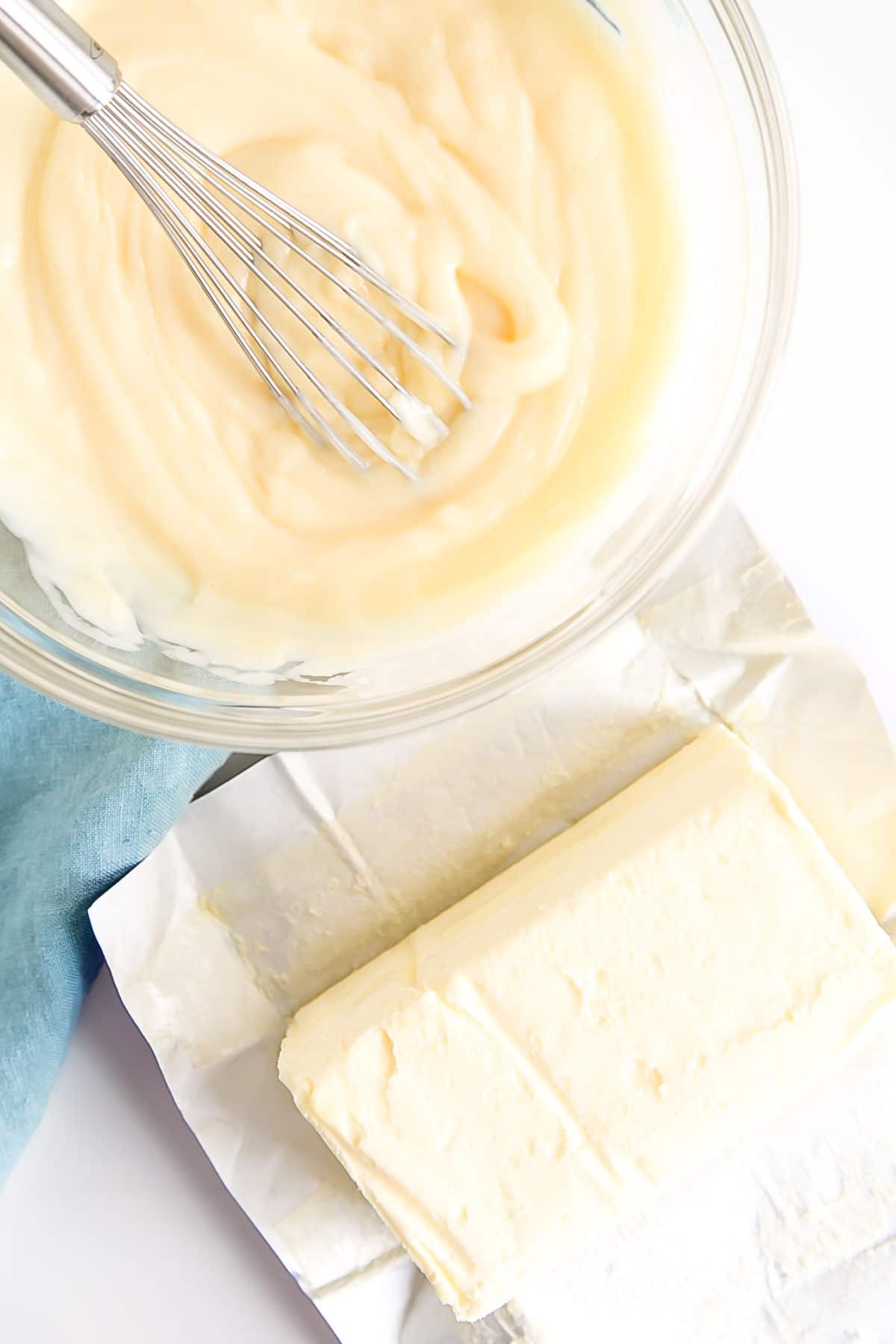 This custard-based German buttercream is made with just a few simple ingredients. Perfect for those who like a rich and silky frosting that isn't too sweet! | livforcake.com Pastry cream in a bowl with a whisk and butter next to it.