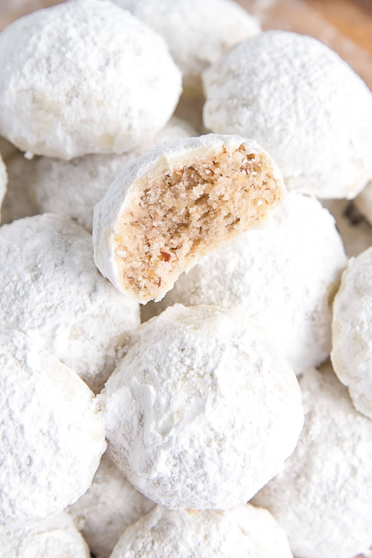 These Mexican Wedding Cookies (also known as Snowball Cookies or Russian Tea Cakes) are buttery, melt-in-your-mouth delicious! Pecan cookies with a hint of cinnamon dusted with powdered sugar. | livforcake.com Close up of half of a mexican wedding cookie on a stack.