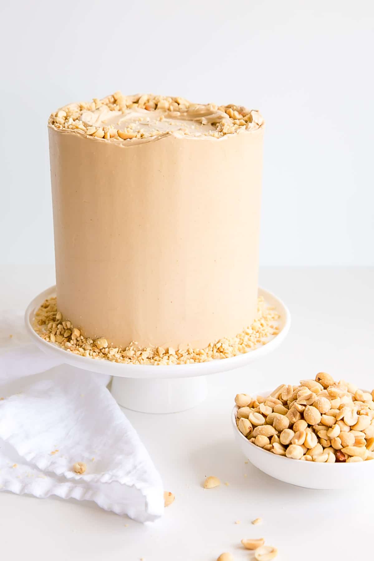 Peanut butter lovers, this cake is for you! Peanut butter cake layers studded with peanut butter chips covered in a peanut butter Swiss meringue buttercream. | livforcake.com Cake on a white cake stand with a bowl of peanuts next to it.
