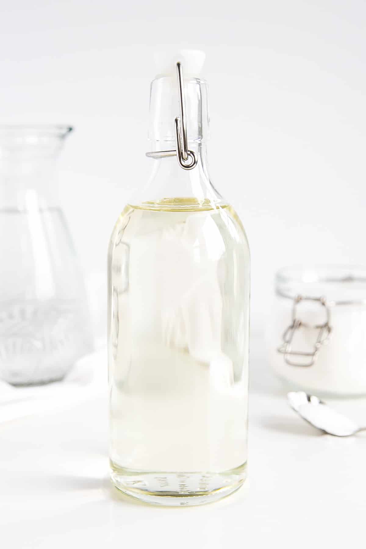 Make simple syrup at home with this quick and easy recipe! The perfect addition to your cakes, cocktails, and iced beverages. | livforcake.com A bottle of homemade simple syrup -- sugar and water in the background.