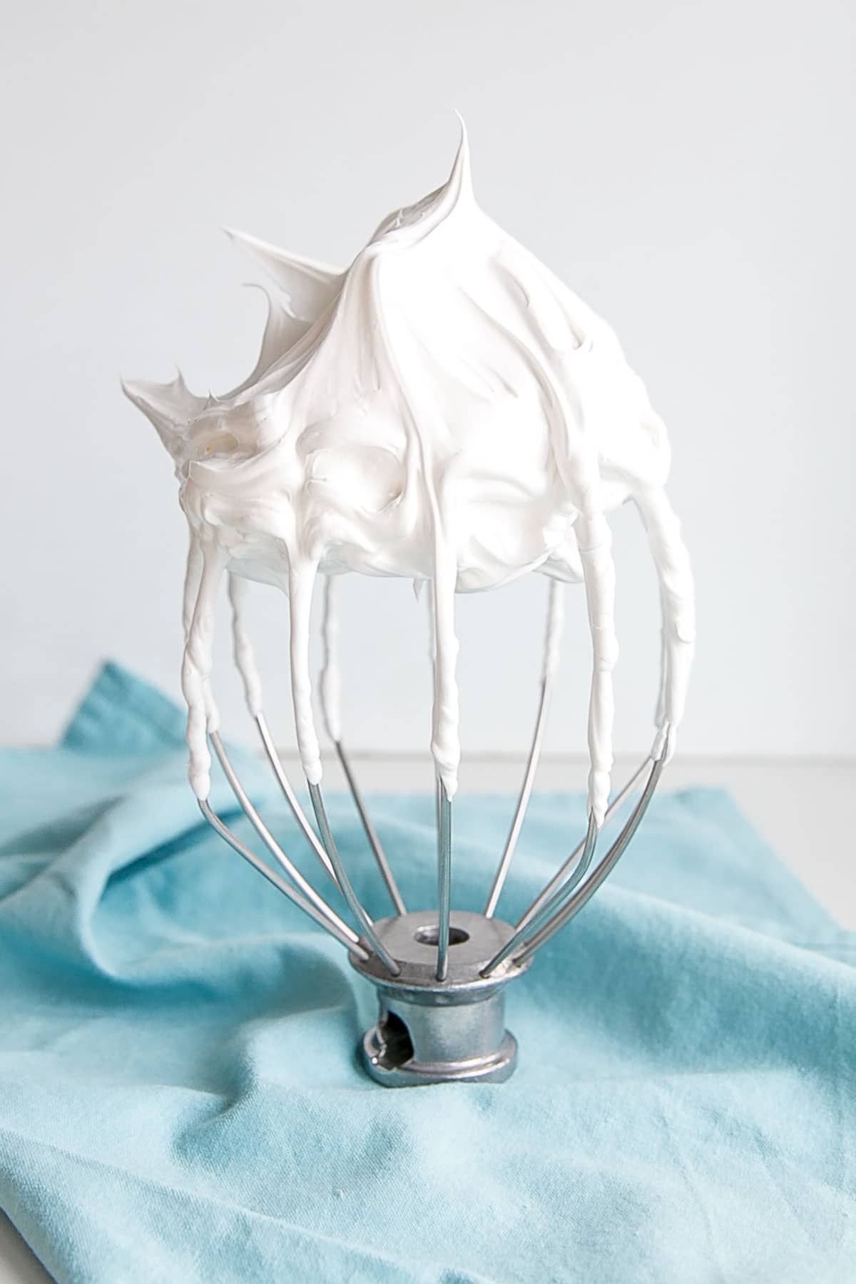 This tutorial on how to make Swiss Meringue buttercream is the only resource you'll need to make the smoothest, silkiest frosting! | livforcake.com Picture of a stiff peak meringue on a stand mixer whisk.