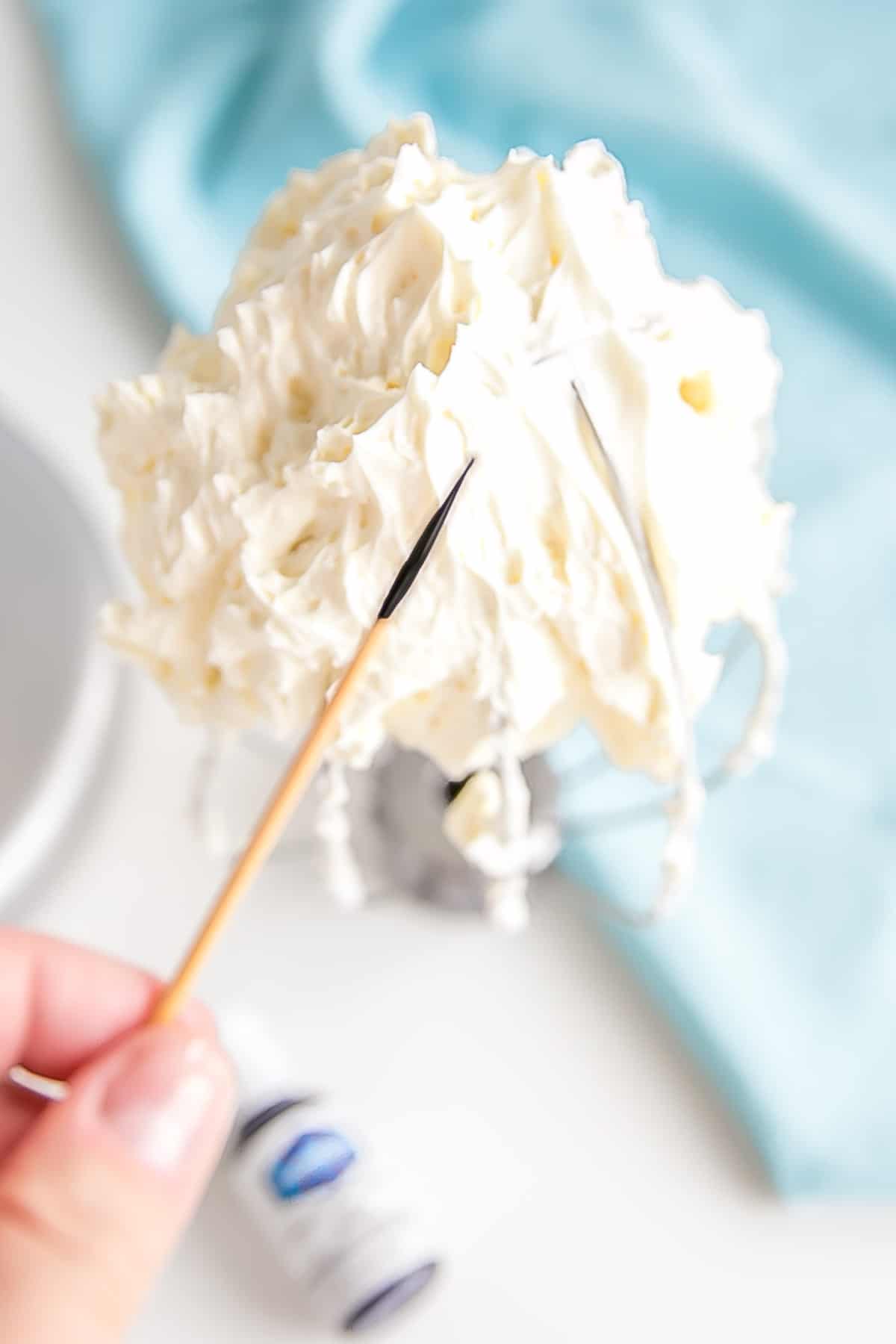 This tutorial on how to make Swiss Meringue buttercream is the only resource you'll need to make the smoothest, silkiest frosting! | livforcake.com Toothpick with violet color gel to help make the buttercream white.