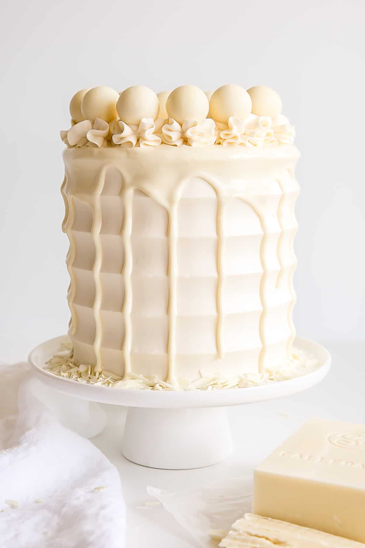 Classic white chocolate cake with scalloped sides, a ganache drip, and truffles on top.