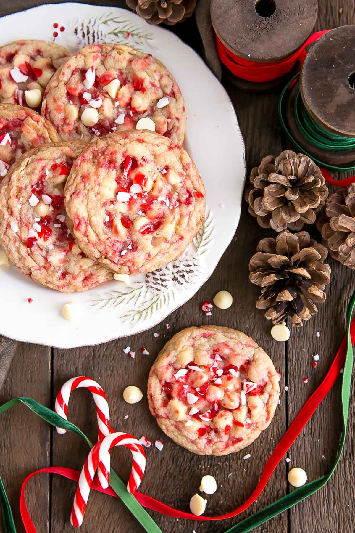 These White Chocolate Candy Cane Cookies are crispy, chewy and delicious. The perfect sweet treat for the holidays! | livforcake.com Overhead shot of White Chocolate Candy Cane Cookies on a plate with ribbons and pine cones